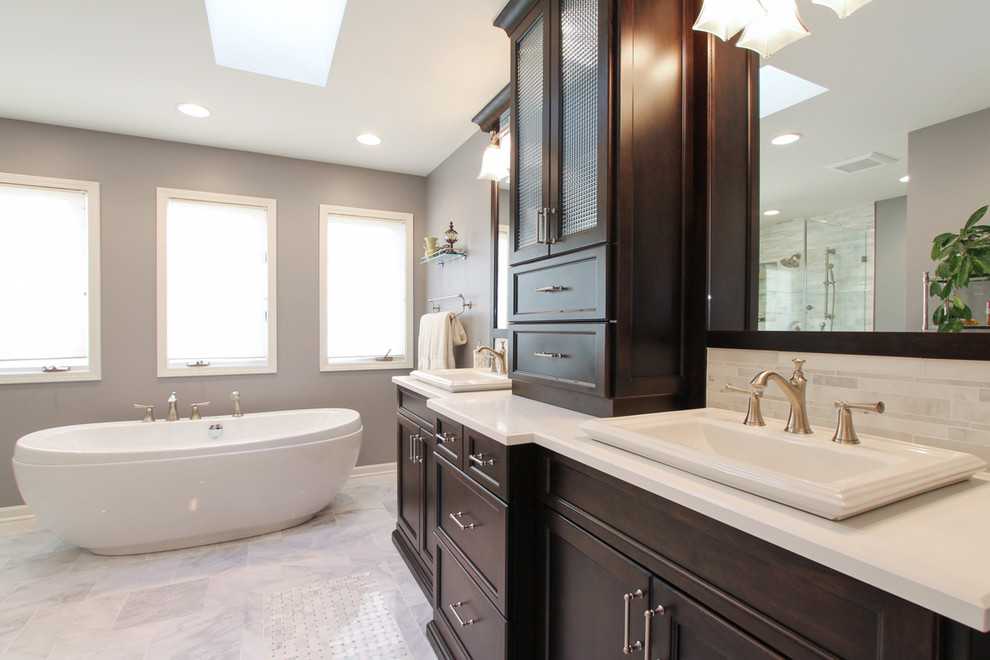 Photo of a large traditional master bathroom in Chicago with a drop-in sink, dark wood cabinets, a freestanding tub, white tile, grey walls, marble floors, shaker cabinets, matchstick tile, engineered quartz benchtops, a corner shower, a two-piece toilet, white floor, a hinged shower door and white benchtops.