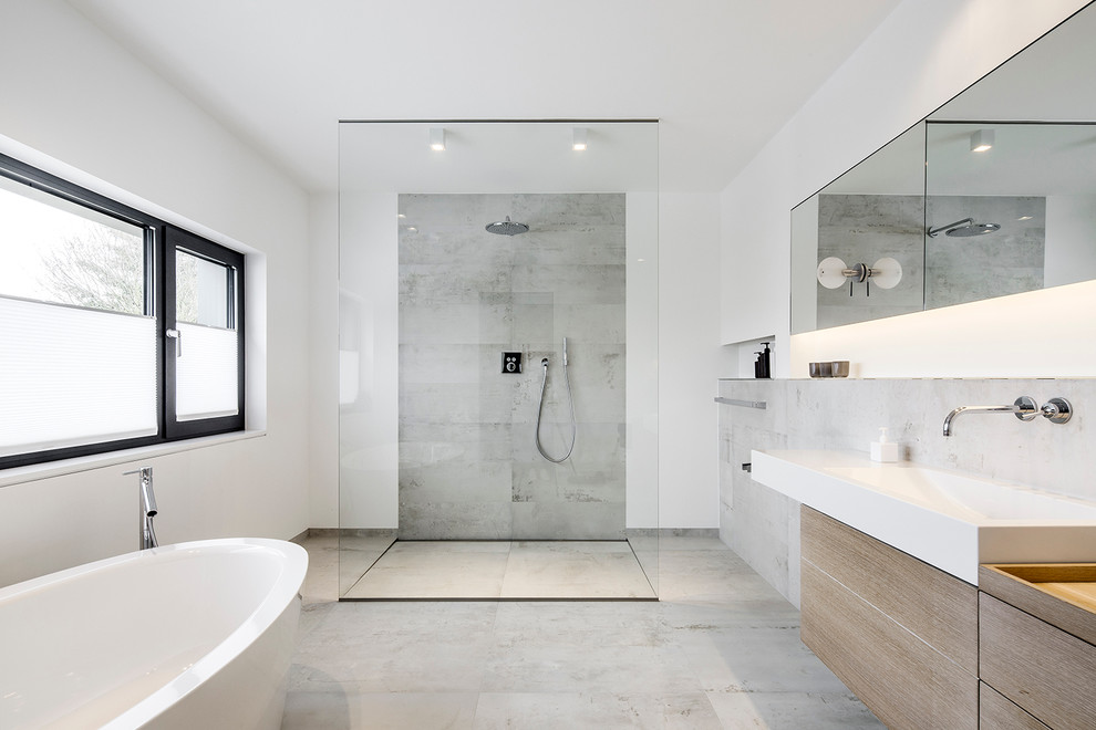 This is an example of a modern master bathroom in Cologne with flat-panel cabinets, a freestanding tub, a curbless shower, gray tile, white walls, medium wood cabinets, concrete floors, a vessel sink and an open shower.