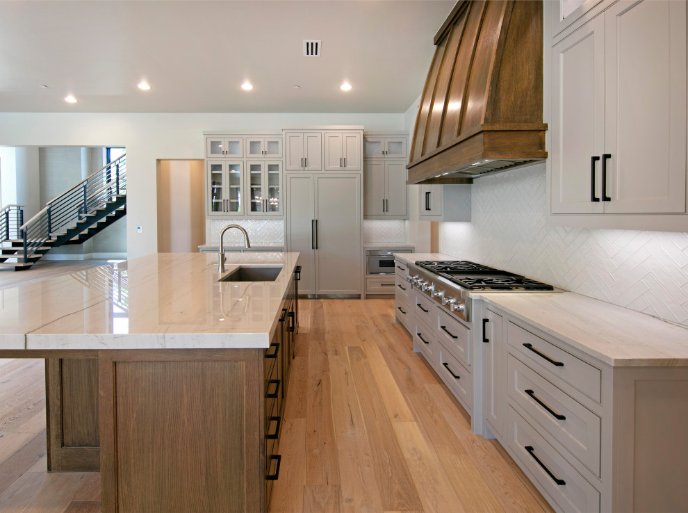 Inspiration for a large transitional u-shaped medium tone wood floor eat-in kitchen remodel in Dallas with an undermount sink, shaker cabinets, gray cabinets, granite countertops, white backsplash, ceramic backsplash, stainless steel appliances, an island and white countertops