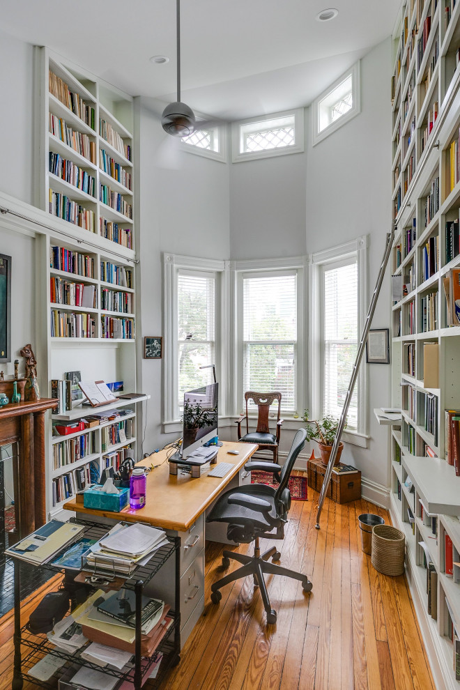 Foto de despacho clásico de tamaño medio con biblioteca, paredes blancas, suelo de madera en tonos medios, todas las chimeneas, marco de chimenea de madera, escritorio independiente y suelo marrón