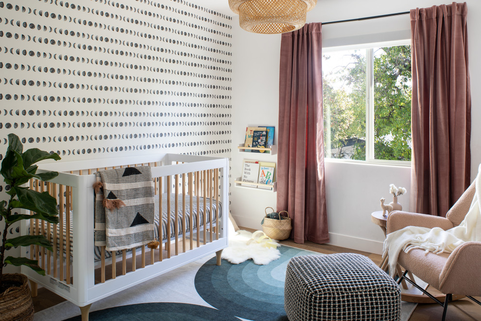 Ejemplo de habitación de bebé niña escandinava de tamaño medio con paredes blancas, suelo de madera clara y papel pintado