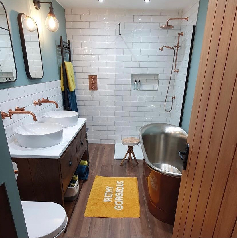 Small modern grey and teal bathroom in Other with brown cabinets, a freestanding bath, a one-piece toilet, white tiles, metro tiles, blue walls, wood-effect flooring, a pedestal sink, brown floors, an open shower, white worktops, feature lighting, double sinks and a freestanding vanity unit.