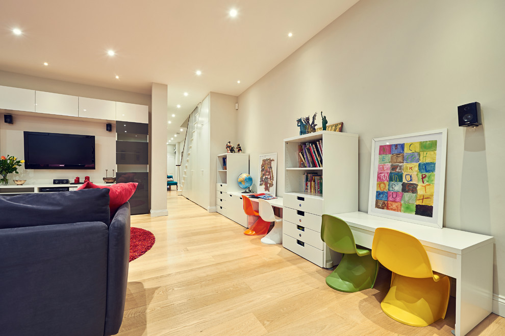 This is an example of a large contemporary gender-neutral kids' playroom for kids 4-10 years old in London with white walls and light hardwood floors.
