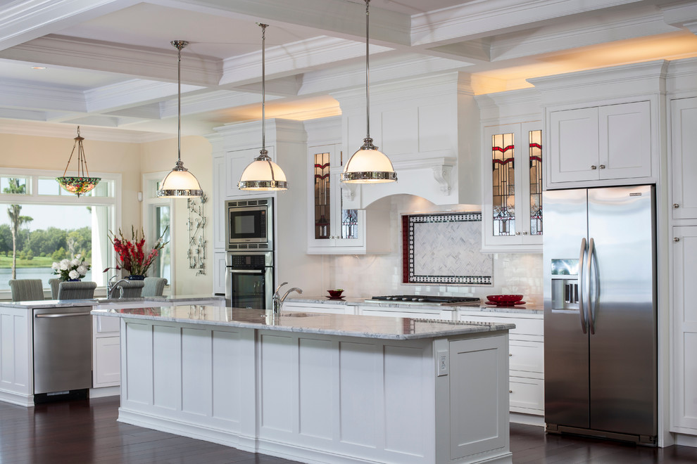 Design ideas for a mid-sized traditional l-shaped open plan kitchen in Orlando with shaker cabinets, white cabinets, marble benchtops, white splashback, stainless steel appliances, glass tile splashback, dark hardwood floors and with island.