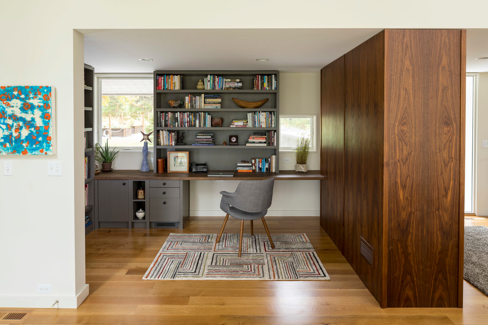 This is an example of a contemporary home office in Minneapolis with white walls, medium hardwood floors, a built-in desk and brown floor.