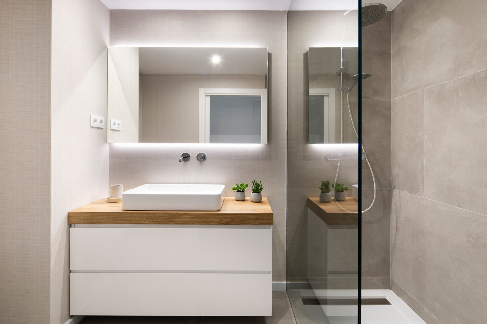 This is an example of a medium sized modern ensuite bathroom in Barcelona with freestanding cabinets, light wood cabinets, a built-in shower, a wall mounted toilet, beige tiles, beige walls, porcelain flooring, a vessel sink, wooden worktops, grey floors, a sliding door, brown worktops, an enclosed toilet, a single sink and a floating vanity unit.