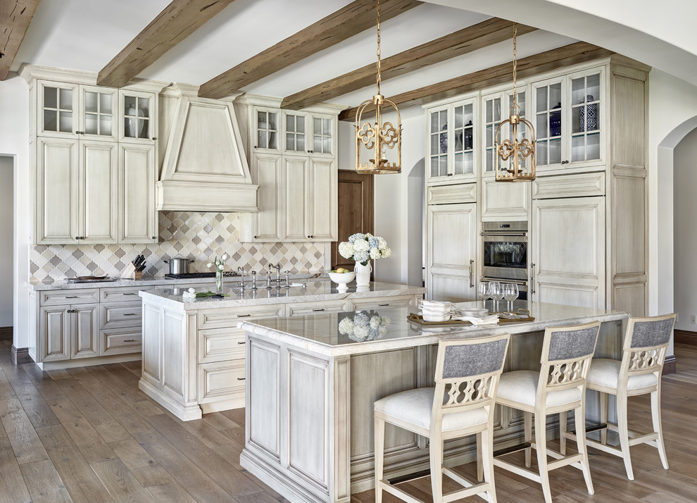 Design ideas for a large mediterranean l-shaped open plan kitchen in Chicago with raised-panel cabinets, light wood cabinets, multi-coloured splashback, panelled appliances, medium hardwood floors, multiple islands, a farmhouse sink, marble benchtops, porcelain splashback and brown floor.