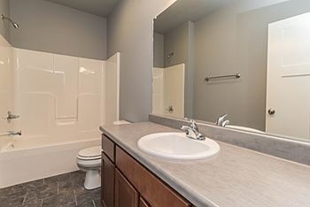 Mid-sized transitional master gray tile and ceramic tile ceramic tile bathroom photo with a drop-in sink, recessed-panel cabinets, medium tone wood cabinets, laminate countertops, a two-piece toilet and gray walls