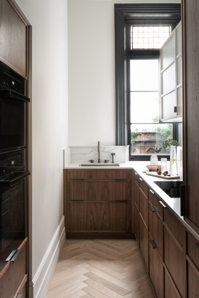 Design ideas for a transitional u-shaped kitchen in London with an undermount sink, flat-panel cabinets, dark wood cabinets, black appliances, medium hardwood floors, no island, brown floor and white benchtop.