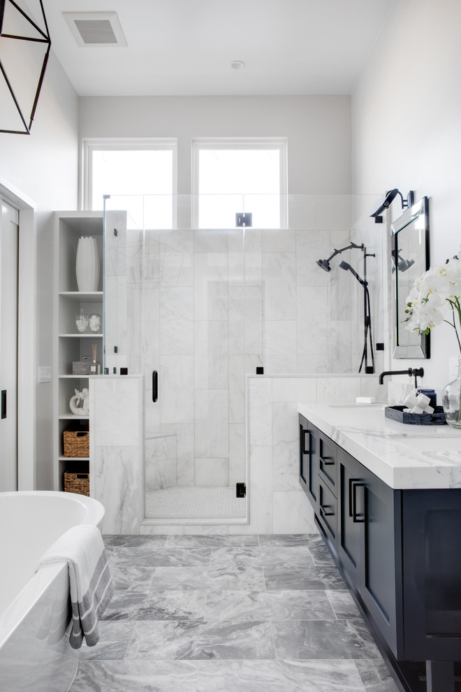 Photo of a mid-sized beach style master bathroom in Los Angeles with shaker cabinets, a freestanding tub, an alcove shower, white tile, white walls, grey floor, a hinged shower door, white benchtops, blue cabinets, a two-piece toilet, marble, marble floors, an undermount sink and engineered quartz benchtops.