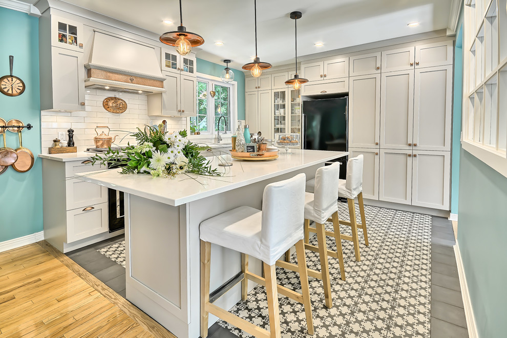 Design ideas for a mid-sized traditional l-shaped kitchen in Montreal with an undermount sink, shaker cabinets, grey cabinets, quartz benchtops, white splashback, subway tile splashback, black appliances, ceramic floors and with island.