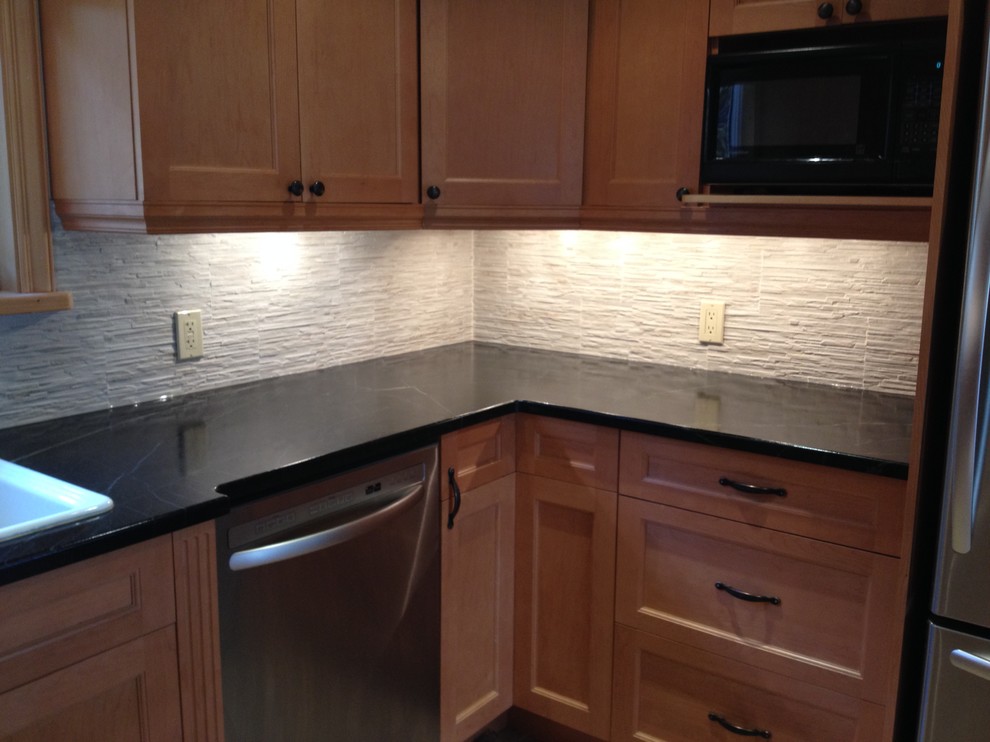 Eat-in kitchen - mid-sized transitional l-shaped brown floor eat-in kitchen idea in Toronto with a drop-in sink, recessed-panel cabinets, medium tone wood cabinets, soapstone countertops, beige backsplash, stone tile backsplash and stainless steel appliances