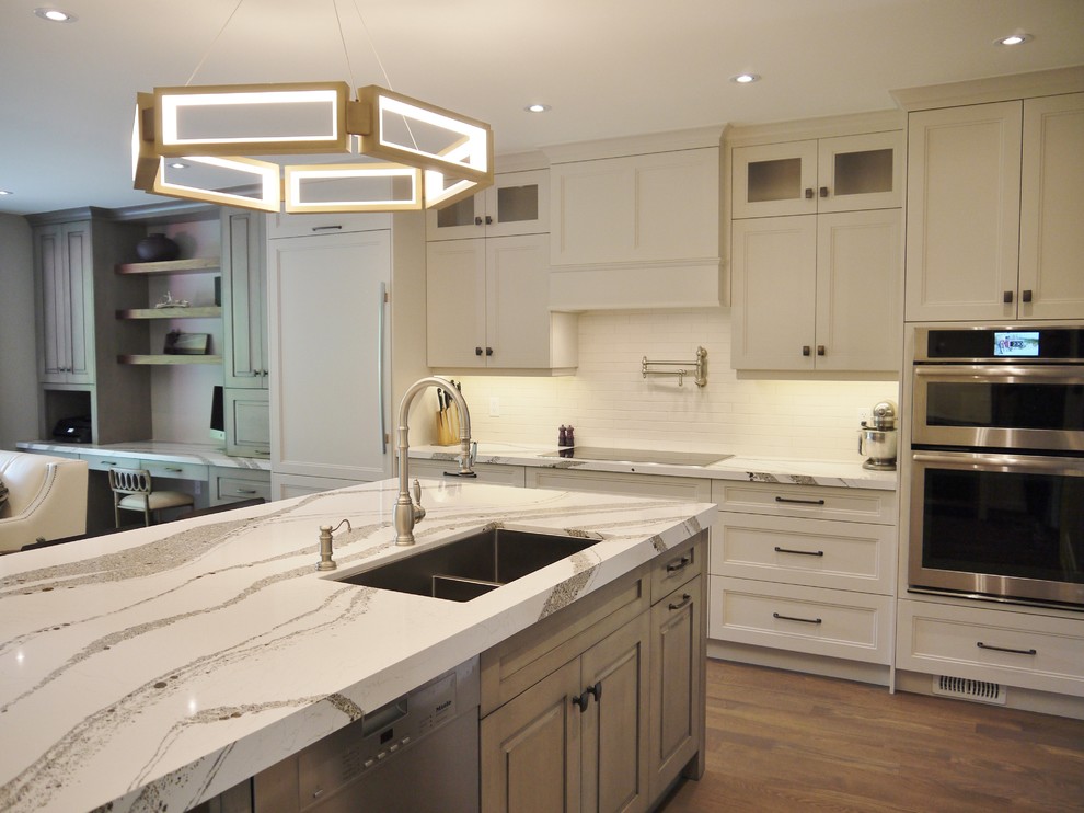 Open concept kitchen - mid-sized transitional medium tone wood floor and brown floor open concept kitchen idea in Toronto with an undermount sink, recessed-panel cabinets, gray cabinets, quartz countertops, white backsplash, porcelain backsplash, stainless steel appliances, an island and white countertops