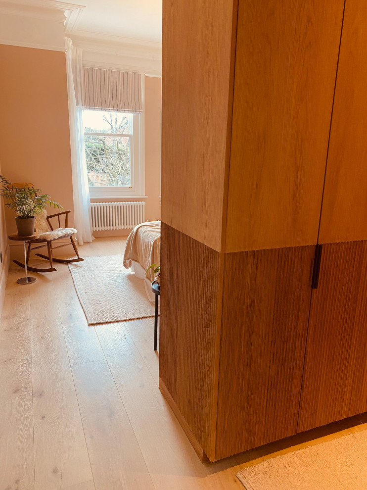 Modelo de dormitorio principal moderno de tamaño medio con paredes rosas, suelo de madera clara, suelo beige y madera