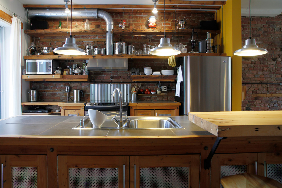 Photo of an industrial galley kitchen in Montreal with a drop-in sink, recessed-panel cabinets, medium wood cabinets, wood benchtops and stainless steel appliances.