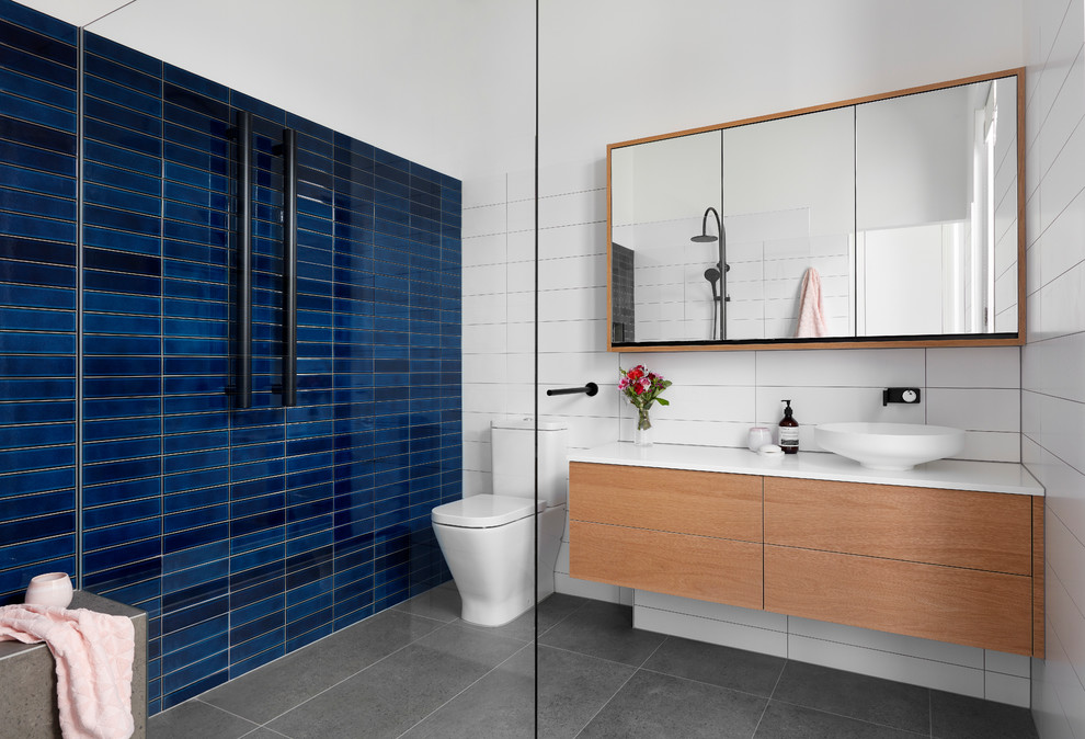 Inspiration for a large contemporary 3/4 wet room bathroom in Melbourne with flat-panel cabinets, medium wood cabinets, a one-piece toilet, blue tile, white walls, a vessel sink, grey floor, an open shower, white benchtops, a freestanding tub and subway tile.