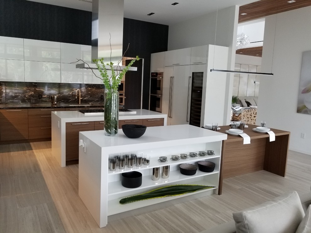 This is an example of a large modern u-shaped eat-in kitchen in Miami with a drop-in sink, flat-panel cabinets, white cabinets, quartz benchtops, black splashback, stainless steel appliances, multiple islands, white benchtop and engineered quartz splashback.