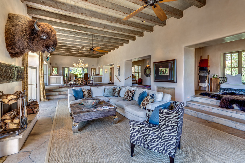 This is an example of an expansive open concept living room in Albuquerque with beige walls, a standard fireplace, a freestanding tv, a plaster fireplace surround and brown floor.