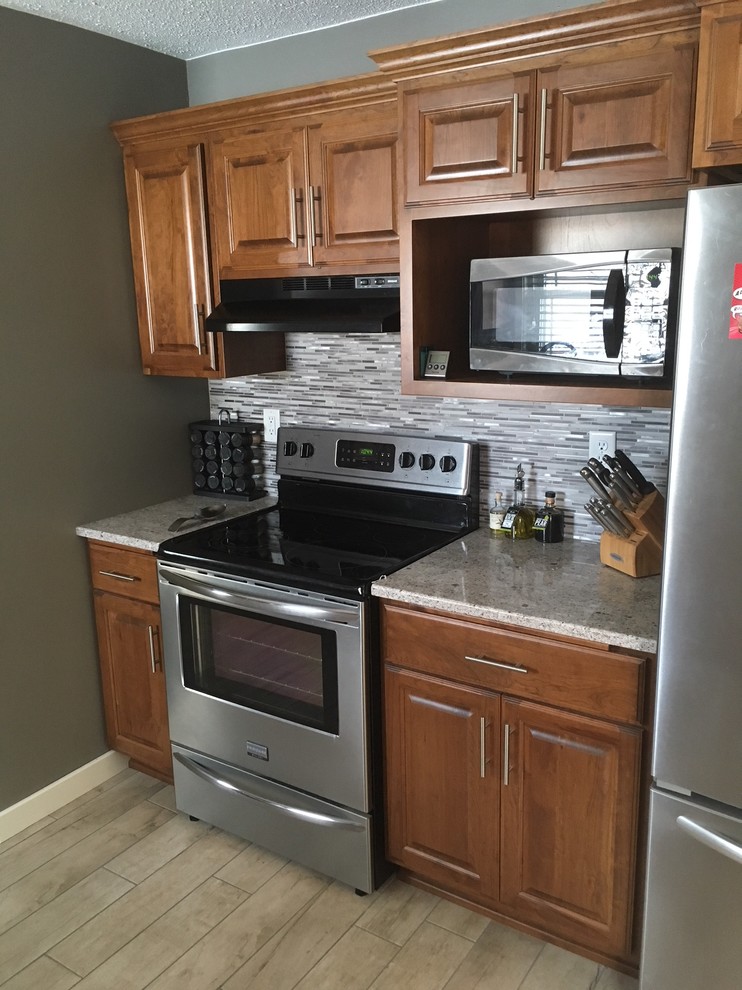 Small transitional single-wall enclosed kitchen photo with raised-panel cabinets, medium tone wood cabinets, quartzite countertops, multicolored backsplash, matchstick tile backsplash and stainless steel appliances