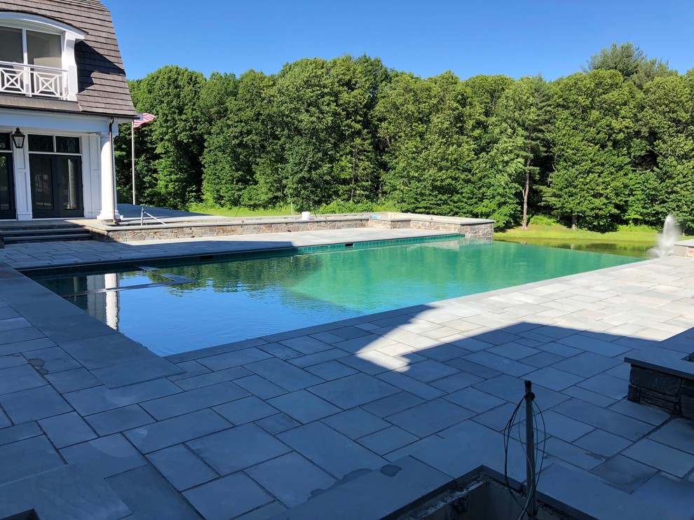 This is an example of a contemporary backyard rectangular infinity pool in New York with with a pool and natural stone pavers.