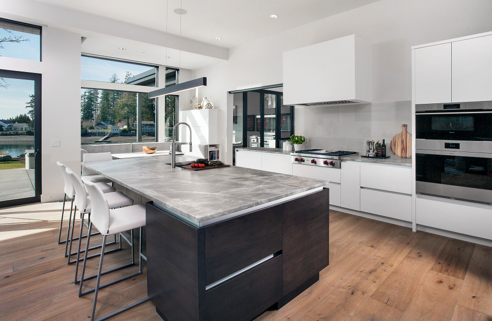 Eat-in kitchen - large contemporary galley medium tone wood floor and brown floor eat-in kitchen idea in Seattle with an undermount sink, flat-panel cabinets, white cabinets, gray backsplash, porcelain backsplash, paneled appliances, an island and gray countertops