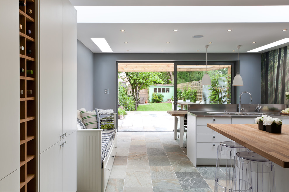 This is an example of a mid-sized contemporary eat-in kitchen in Surrey with an integrated sink, flat-panel cabinets, white cabinets, wood benchtops, white splashback, ceramic splashback, stainless steel appliances and with island.