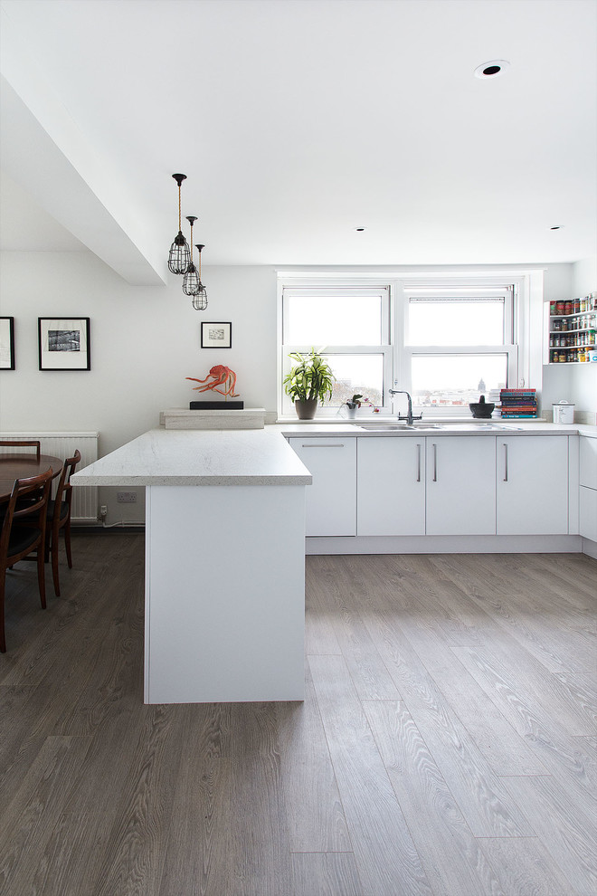 Inspiration for a mid-sized contemporary u-shaped open plan kitchen in Sussex with a drop-in sink, flat-panel cabinets, white cabinets, laminate benchtops, blue splashback, stainless steel appliances, light hardwood floors and a peninsula.