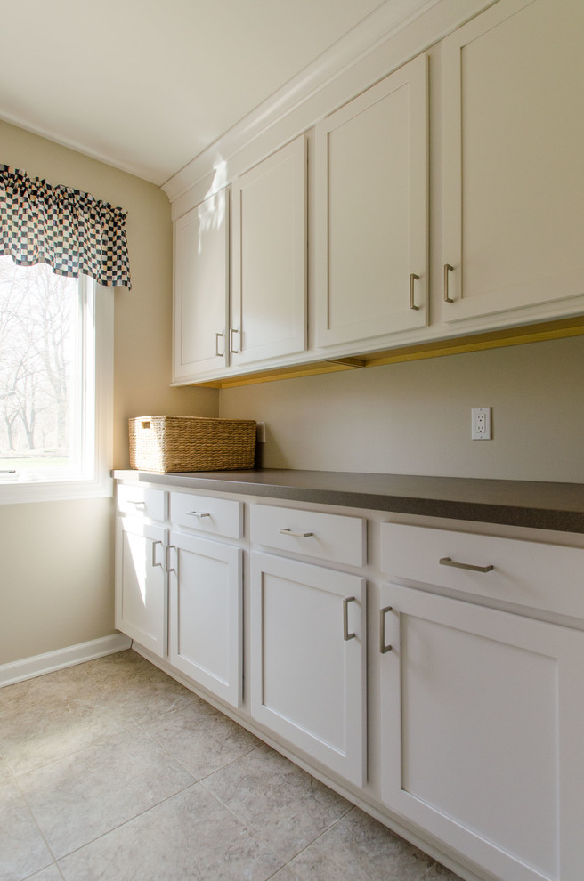 Photo of a mid-sized transitional galley dedicated laundry room in New York with recessed-panel cabinets, white cabinets, laminate benchtops, beige walls, ceramic floors and a side-by-side washer and dryer.