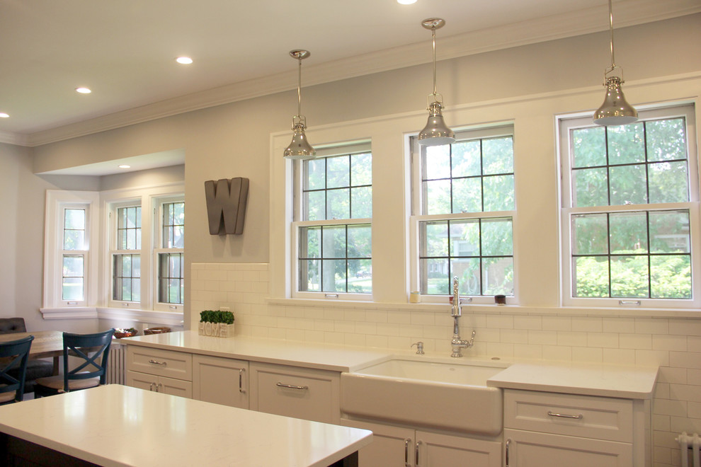 Inspiration for a mid-sized transitional u-shaped medium tone wood floor and brown floor eat-in kitchen remodel with a farmhouse sink, shaker cabinets, white cabinets, quartz countertops, white backsplash, subway tile backsplash, white appliances and an island