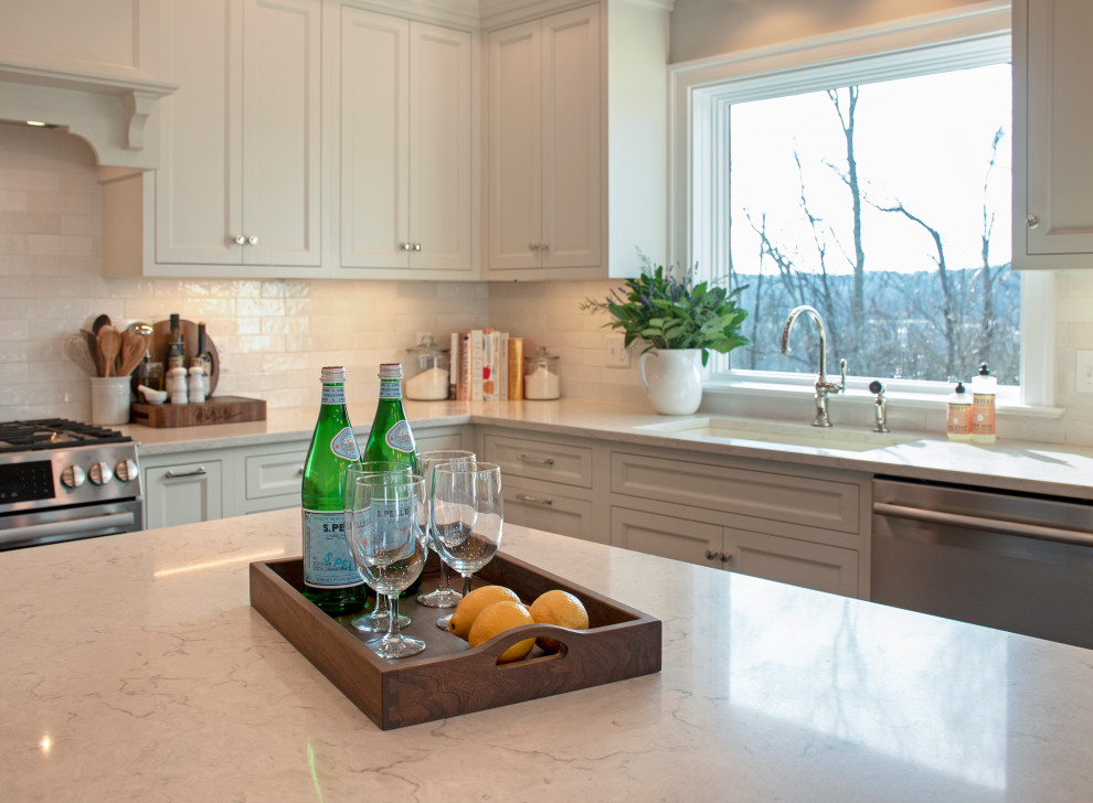 Example of a transitional eat-in kitchen design with an undermount sink, shaker cabinets, white cabinets, quartz countertops, white backsplash, ceramic backsplash, stainless steel appliances, an island and white countertops