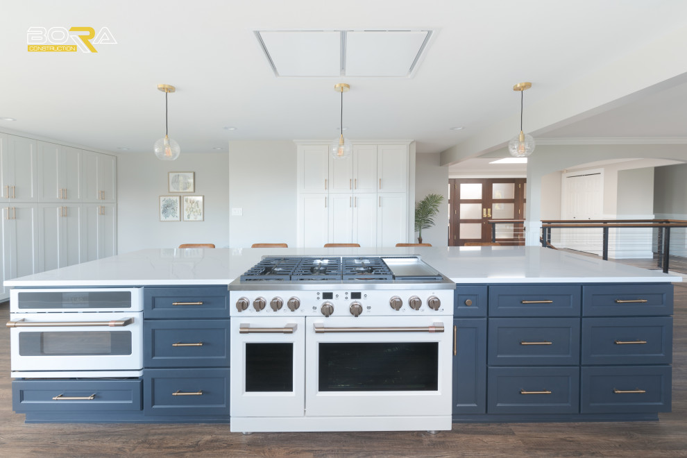 Eat-in kitchen - huge transitional galley medium tone wood floor and brown floor eat-in kitchen idea in Seattle with an undermount sink, shaker cabinets, white cabinets, quartz countertops, white backsplash, ceramic backsplash, white appliances, an island and white countertops