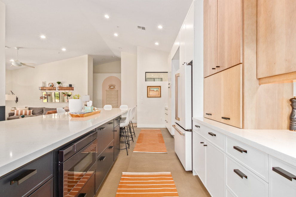 This is an example of a large midcentury eat-in kitchen in Phoenix with an undermount sink, shaker cabinets, white cabinets, quartz benchtops, white splashback, engineered quartz splashback, white appliances, concrete floors, with island and white benchtop.