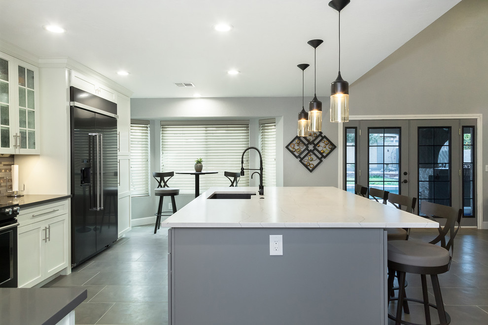 Open concept kitchen - mid-sized transitional l-shaped porcelain tile and gray floor open concept kitchen idea in Phoenix with an undermount sink, shaker cabinets, white cabinets, quartz countertops, gray backsplash, glass tile backsplash, black appliances, an island and gray countertops