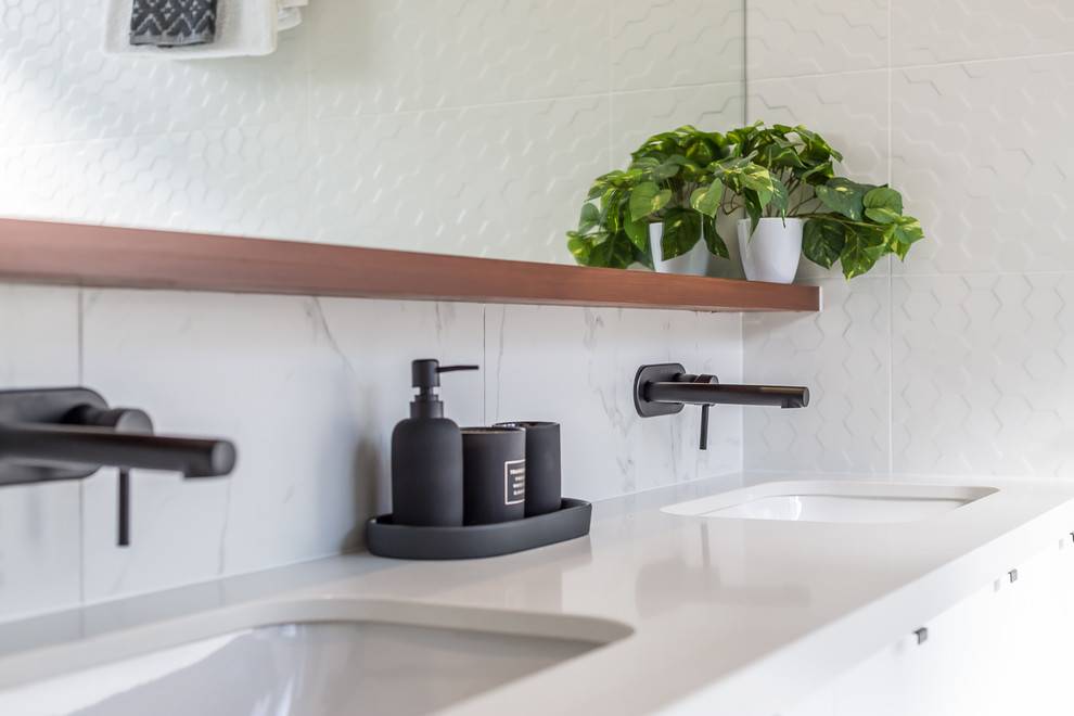 This is an example of a mid-sized contemporary 3/4 bathroom in Brisbane with white cabinets, a freestanding tub, a corner shower, a two-piece toilet, white tile, ceramic tile, white walls, ceramic floors, an undermount sink, engineered quartz benchtops, white floor, a hinged shower door and white benchtops.