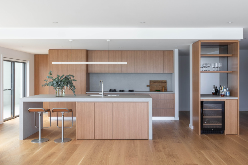 Mid-sized contemporary galley kitchen in Sydney with an undermount sink, flat-panel cabinets, light wood cabinets, panelled appliances, medium hardwood floors, with island, brown floor and grey benchtop.