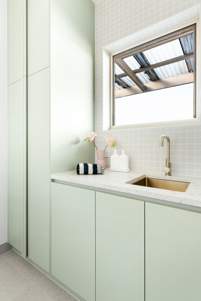Imagen de lavadero lineal actual de tamaño medio con puertas de armario verdes, encimera de terrazo, salpicadero gris, paredes blancas, lavadora y secadora apiladas y encimeras blancas