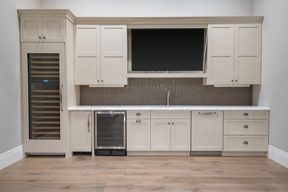 This is an example of a large contemporary single-wall wet bar in Phoenix with an integrated sink, beige cabinets, marble benchtops, grey splashback, medium hardwood floors, brown floor, grey benchtop and recessed-panel cabinets.