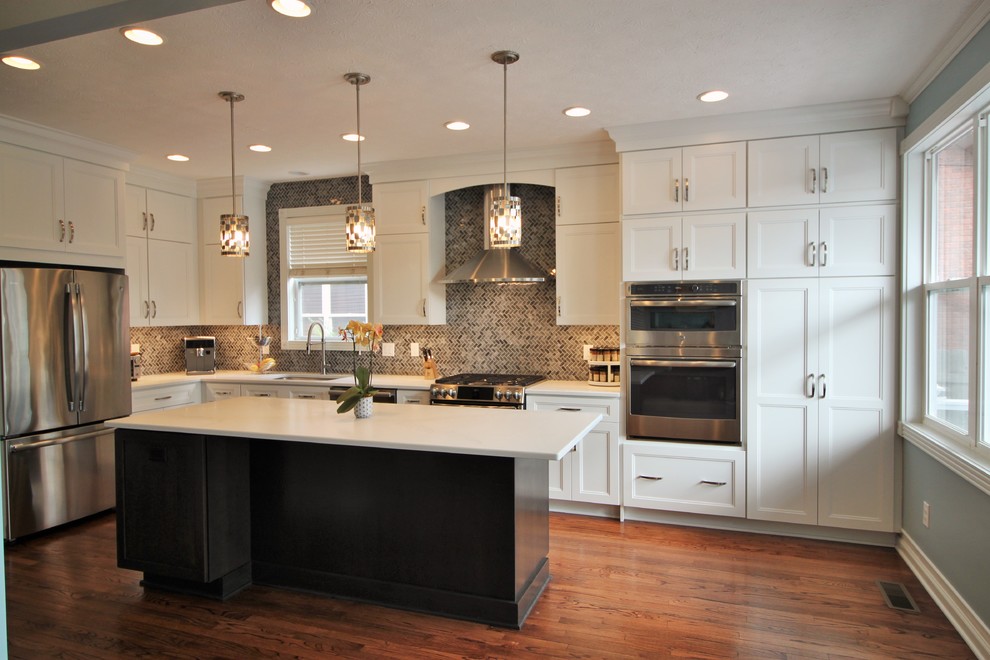 Design ideas for a mid-sized transitional l-shaped kitchen in Indianapolis with an undermount sink, shaker cabinets, white cabinets, quartz benchtops, grey splashback, mosaic tile splashback, stainless steel appliances, medium hardwood floors, with island and white benchtop.