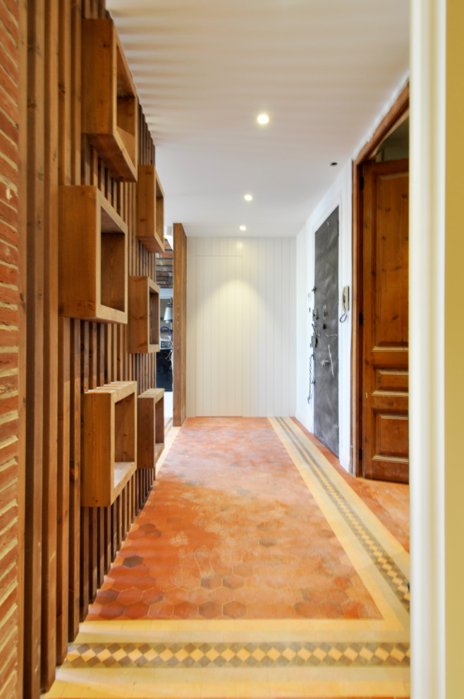 На фото: большая узкая прихожая в стиле модернизм с белыми стенами, полом из керамической плитки, одностворчатой входной дверью, металлической входной дверью, серым полом, сводчатым потолком и кирпичными стенами с