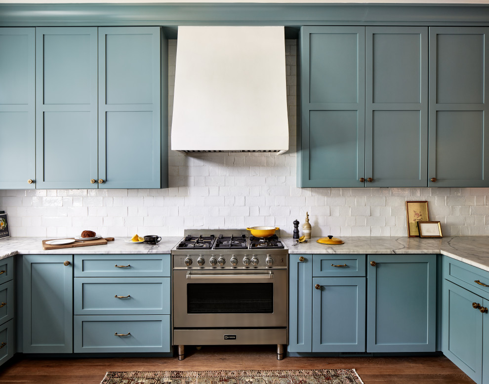 Cette photo montre une grande cuisine américaine chic avec un placard à porte shaker, des portes de placard bleues, plan de travail en marbre et une crédence blanche.
