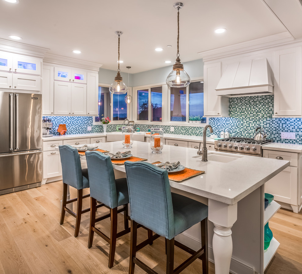 This is an example of a transitional l-shaped kitchen in San Diego with a farmhouse sink, shaker cabinets, white cabinets, blue splashback, mosaic tile splashback, stainless steel appliances, medium hardwood floors and with island.