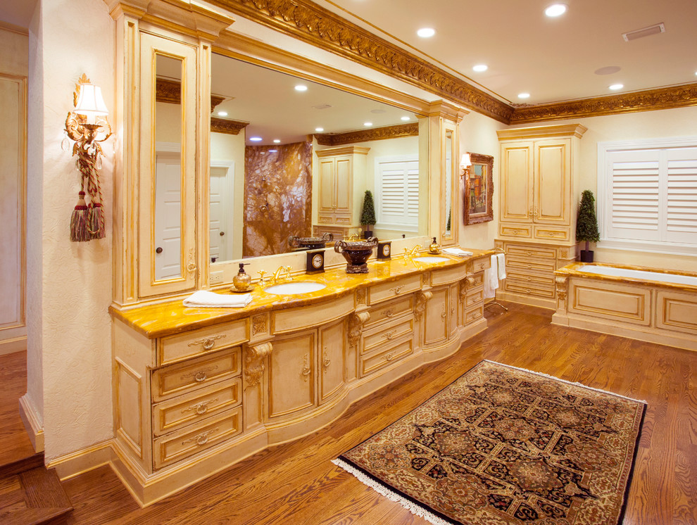 This is an example of an expansive mediterranean master bathroom in Tampa with an undermount sink, furniture-like cabinets, distressed cabinets, marble benchtops, an undermount tub, an open shower, beige walls, medium hardwood floors and brown floor.