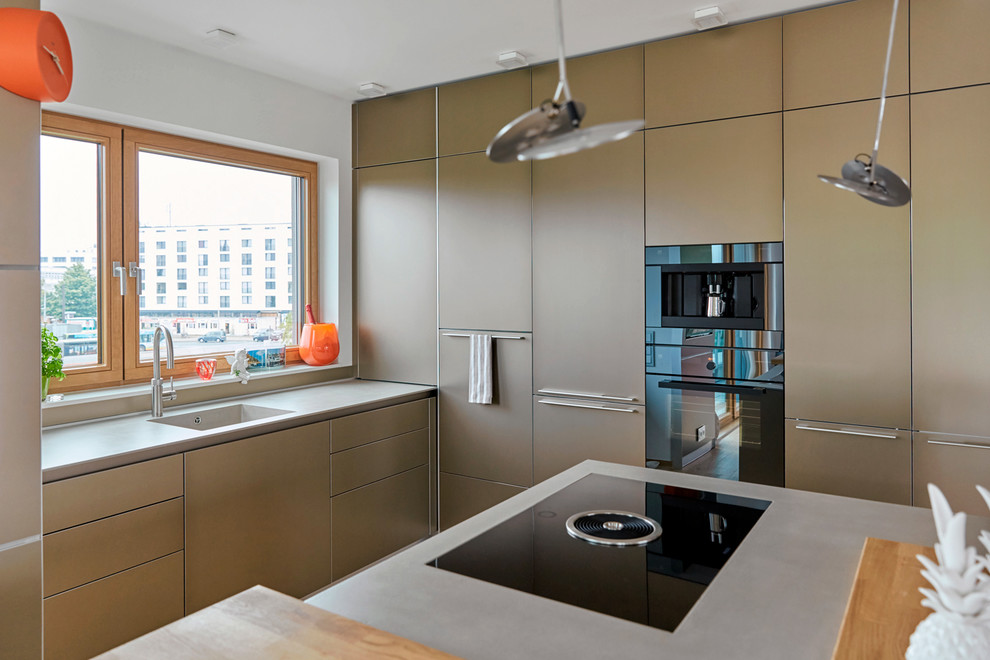 Modern inredning av ett kök, med en enkel diskho, släta luckor, bänkskiva i betong, svarta vitvaror, mellanmörkt trägolv och en köksö