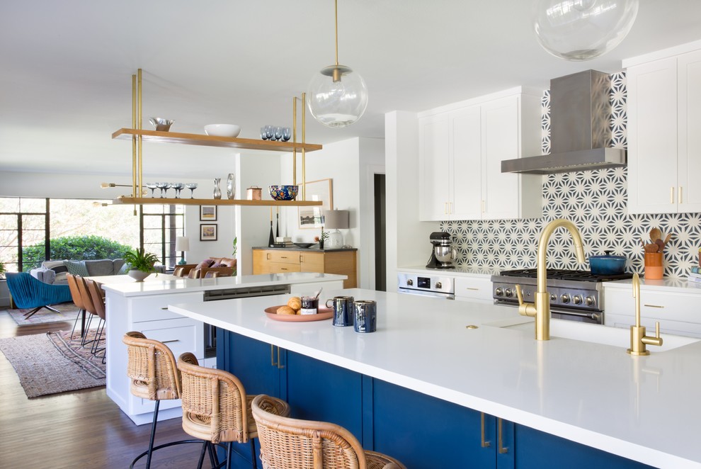 This is an example of an eclectic open plan kitchen in Austin with a farmhouse sink, shaker cabinets, blue cabinets, multi-coloured splashback, mosaic tile splashback, stainless steel appliances, dark hardwood floors, multiple islands and brown floor.