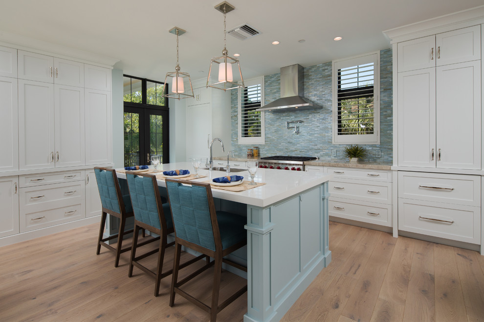 This is an example of a beach style kitchen in Miami with an undermount sink, shaker cabinets, white cabinets, blue splashback, mosaic tile splashback, stainless steel appliances, light hardwood floors, with island, beige floor and white benchtop.