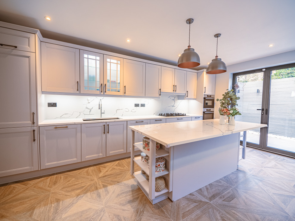 Large traditional single-wall eat-in kitchen in London with a double-bowl sink, shaker cabinets, quartzite benchtops, white splashback, engineered quartz splashback, stainless steel appliances, ceramic floors, with island, brown floor and white benchtop.
