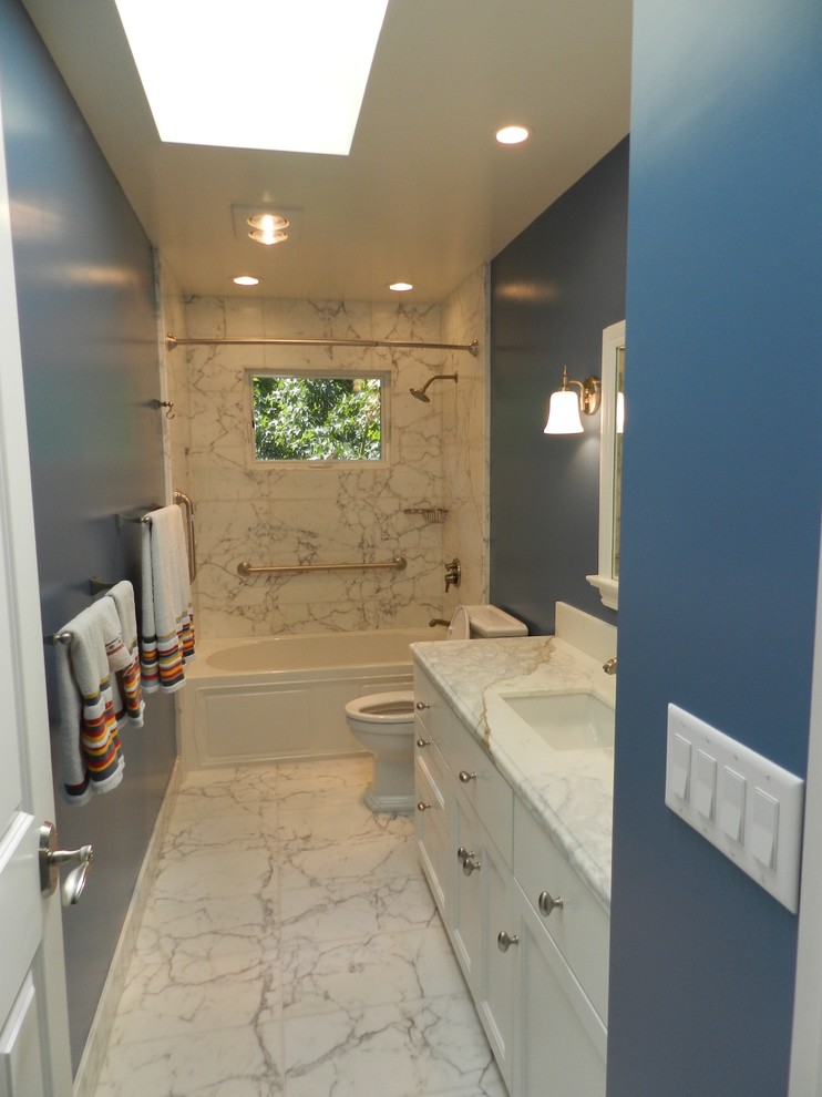 Design ideas for a mid-sized eclectic bathroom in San Francisco with recessed-panel cabinets, an alcove tub, a shower/bathtub combo, a two-piece toilet, black and white tile, stone tile, blue walls, marble floors, an undermount sink and marble benchtops.