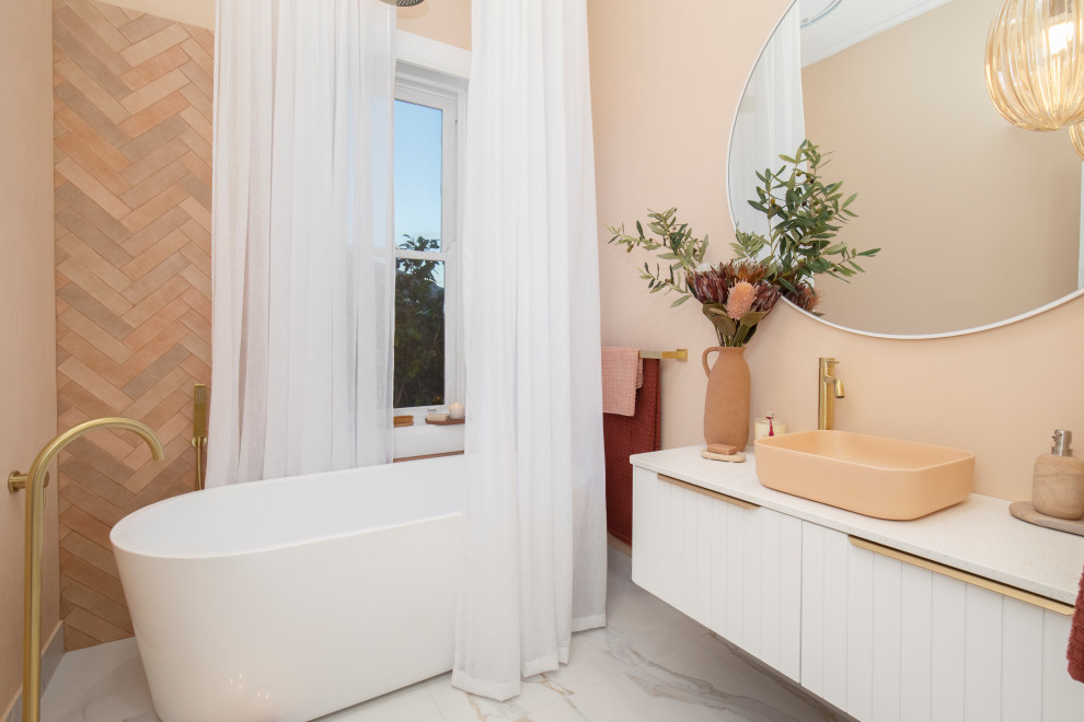This is an example of a small contemporary ensuite bathroom in Newcastle - Maitland with white cabinets, a freestanding bath, a shower/bath combination, a one-piece toilet, orange tiles, ceramic tiles, orange walls, marble flooring, a vessel sink, engineered stone worktops, white floors, a shower curtain, white worktops, a single sink, a floating vanity unit and all types of wall treatment.