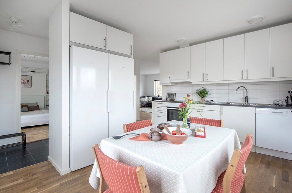 Exempel på ett minimalistiskt kök och matrum, med släta luckor, vita skåp, vitt stänkskydd, vita vitvaror, mellanmörkt trägolv och beiget golv