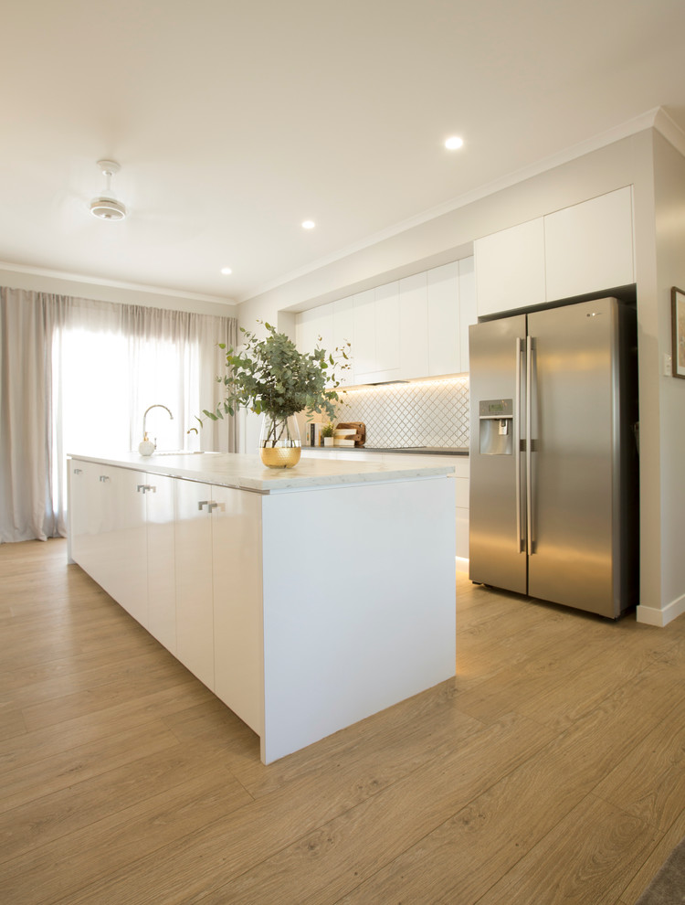 Mid-sized contemporary galley eat-in kitchen in Townsville with a single-bowl sink, flat-panel cabinets, white cabinets, laminate benchtops, white splashback, ceramic splashback, stainless steel appliances, vinyl floors and with island.